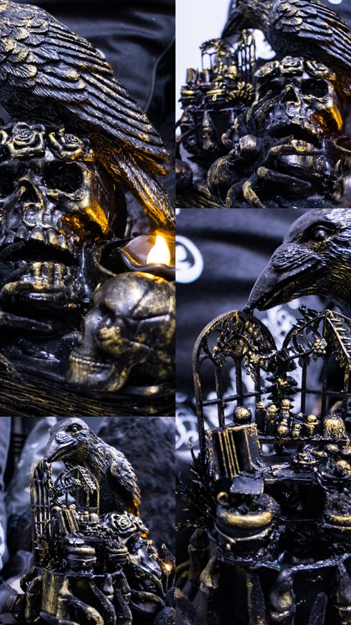 Skulptur eines Raben auf Totenköpfen vor einem gotischen Fenster